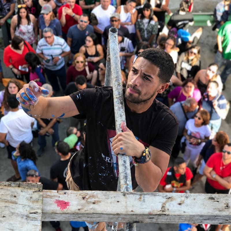 A man with blue paint on his hands holds a metal pole in the foreground, while a crowd of people watches in the background.