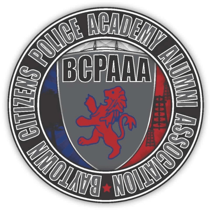 A red lion rampant is centered on a shield with "BCPAAA" above it, all within a circular emblem featuring "CITIZENS POLICE ACADEMY ALUMNI ASSOCIATION BAYTOWN" around the edge, with a stylized cityscape in the background.