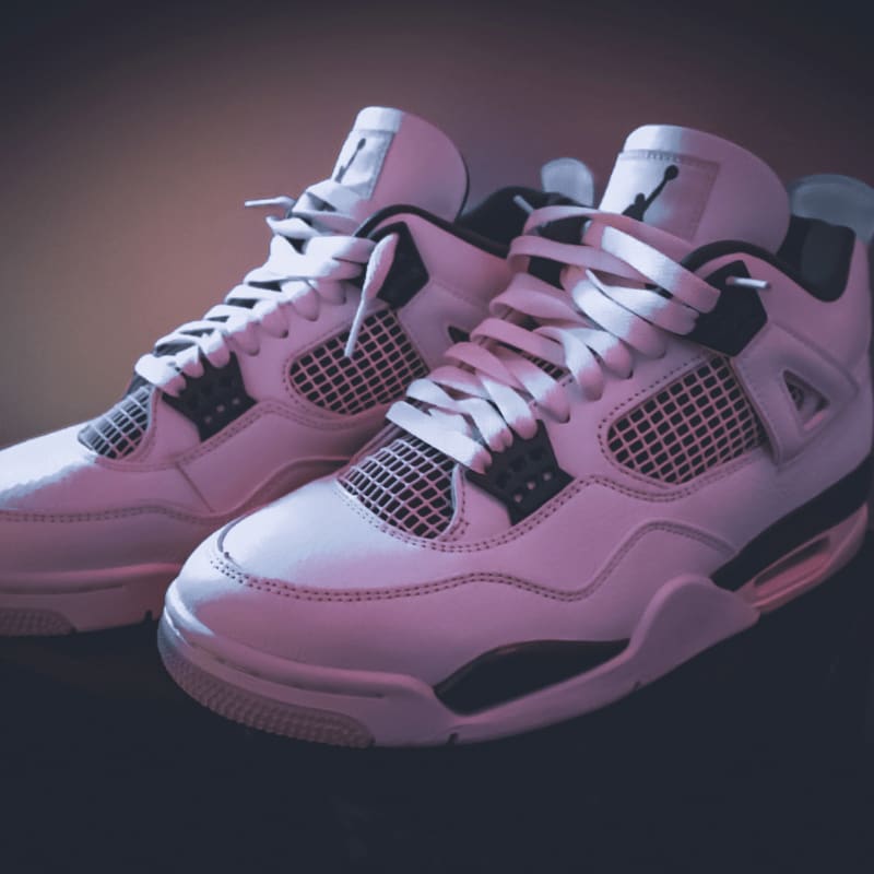 A pair of white sneakers with black accents rests on a dark surface, with a softly lit, blurred background.