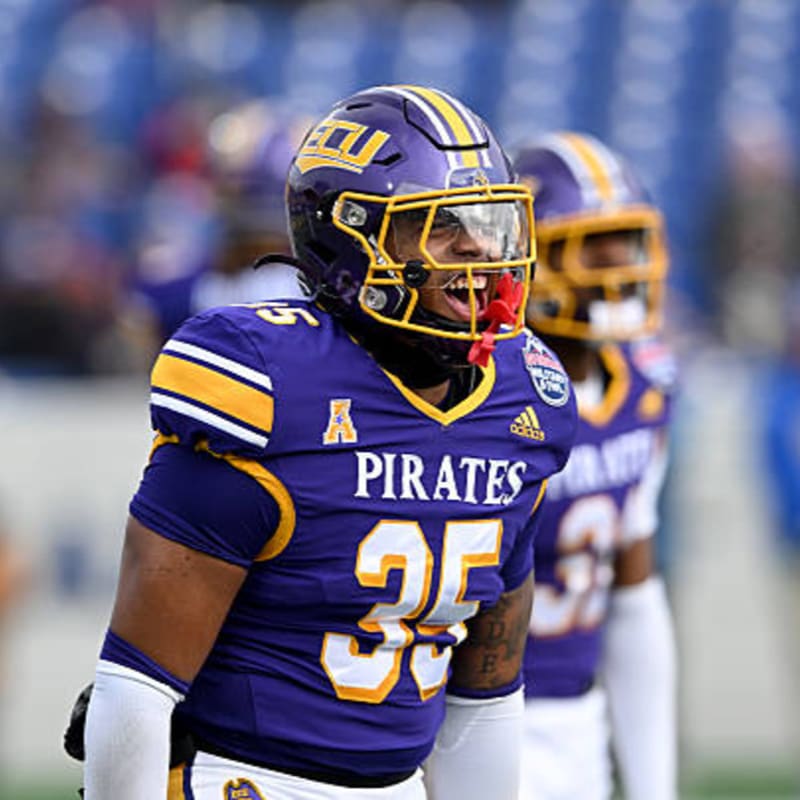 A football player in a purple "Pirates" jersey with the number 35 is in the foreground, while another player in a similar uniform is blurred in the background.