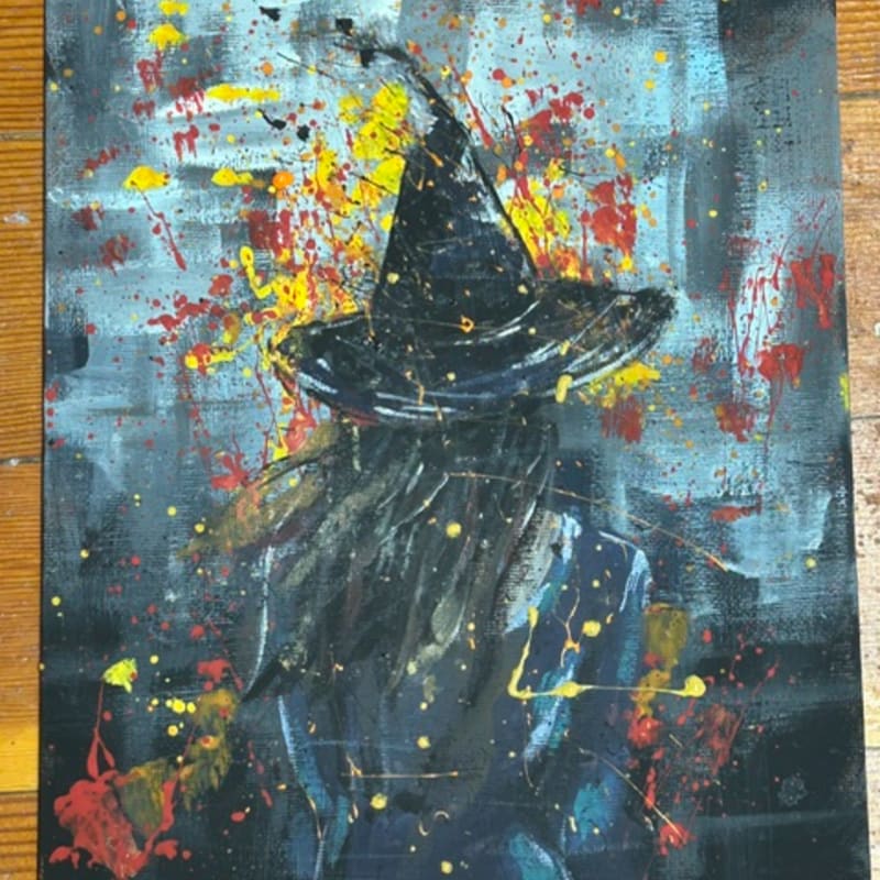 A person in a witch hat is depicted in the foreground with a chaotic, splattered background.