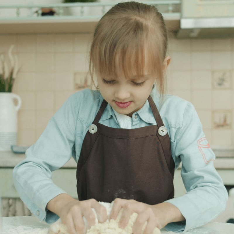 Young girl wearing apron kneading dough in kitchen.