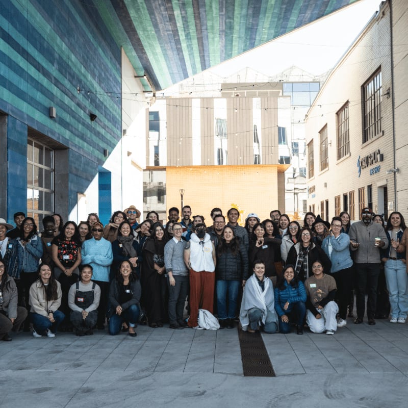 A large group of people pose for a photo in an urban courtyard with colorful buildings in the background.