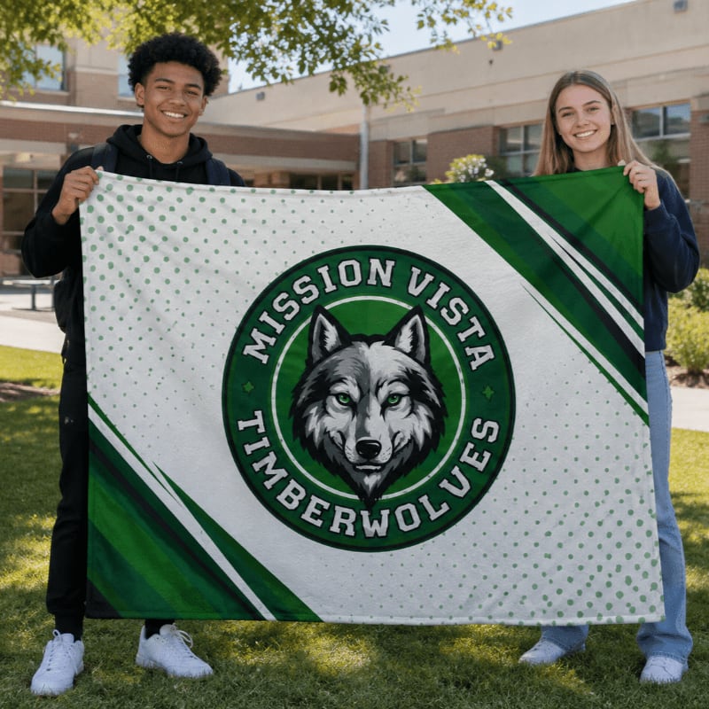 Two smiling teenagers hold up a large blanket with a wolf mascot in front of a school building.