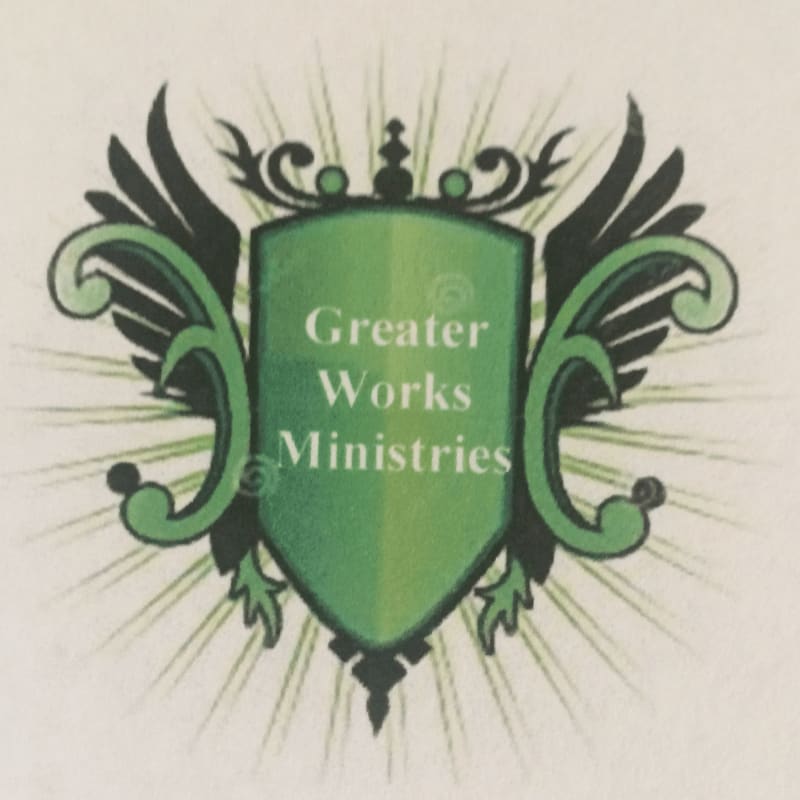 A green shield with "Greater Works Ministries" written on it is surrounded by ornate green wings and a radiating light effect against a cream-colored background.