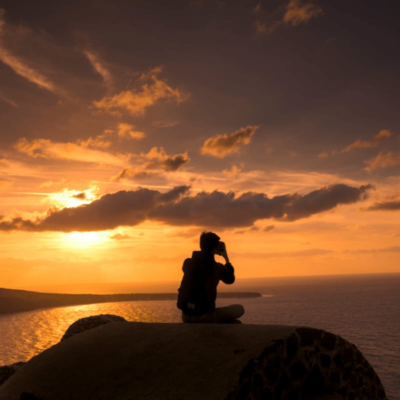 silhouette of person sitting on hill near body of water