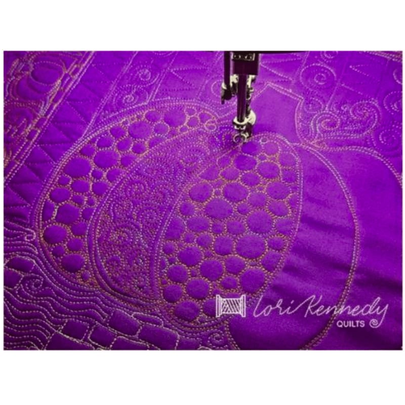 A sewing machine's needle stitches a detailed pumpkin design onto vibrant purple fabric, with intricate quilting patterns visible in the background.