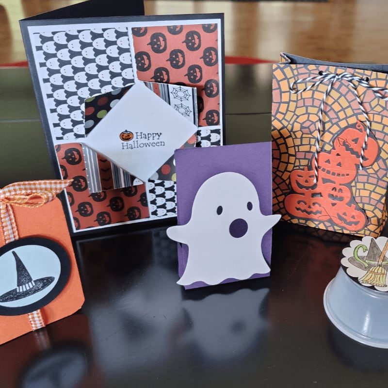 A white ghost cutout stands in front of a Halloween card and gift bag, with a small orange gift box to the left.