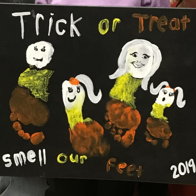 Four footprint figures with painted faces and bodies stand on a black background with the words "Trick or Treat smell our Feet" and "2019" written in white and orange.