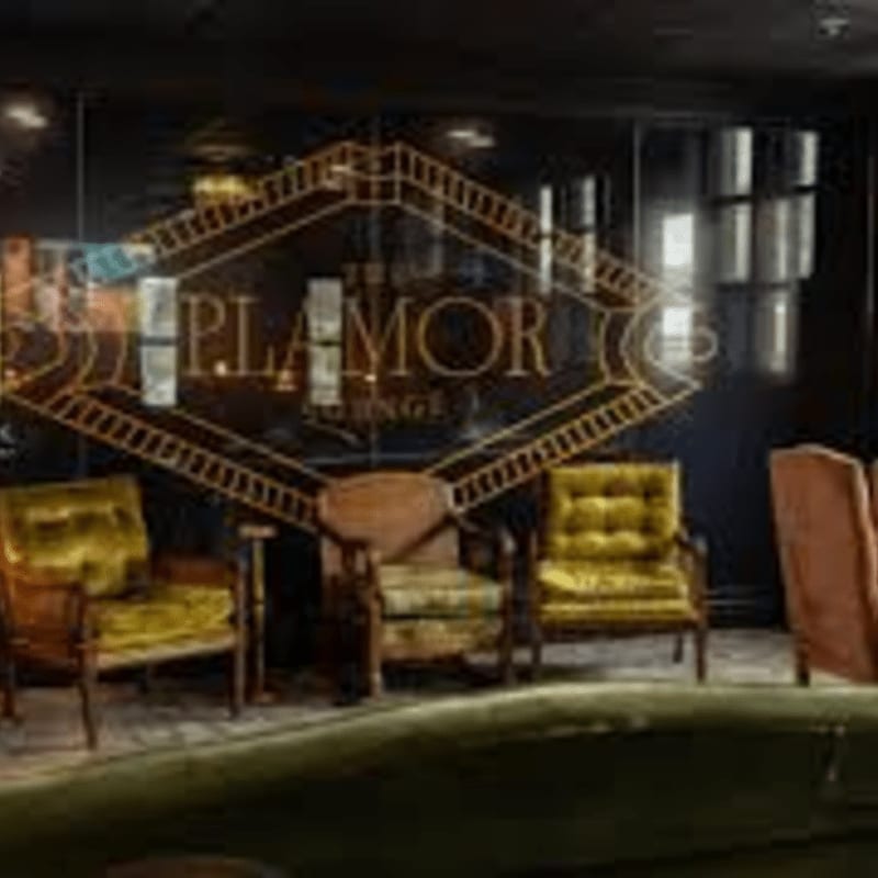 Plush velvet armchairs are arranged in front of a large, illuminated "The Glamor Lounge" sign set against a dark, reflective background.