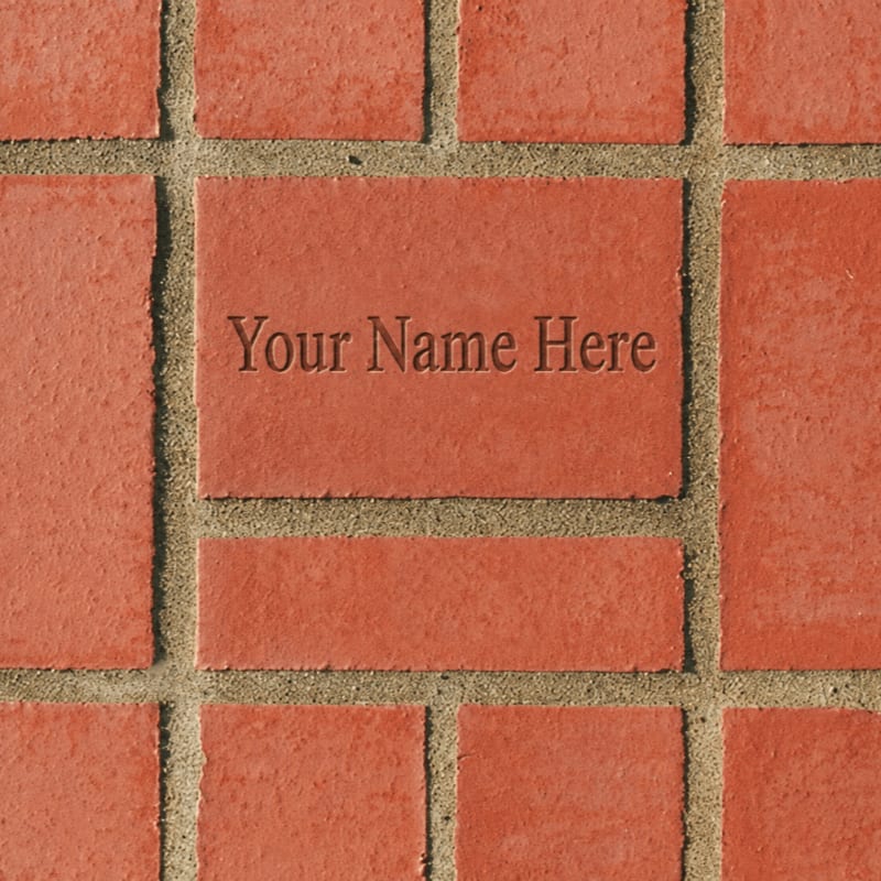 A personalized brick with "Your Name Here" engraved is set within a textured brick pathway.
