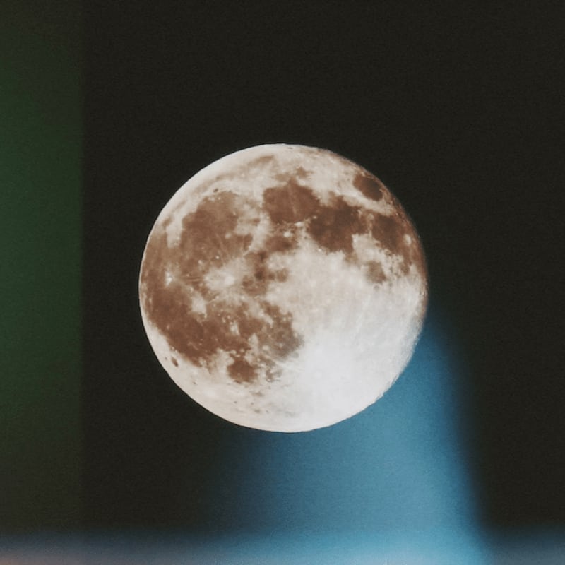 A full moon with visible craters glows against a dark, starry background with a faint blue light emanating from below.