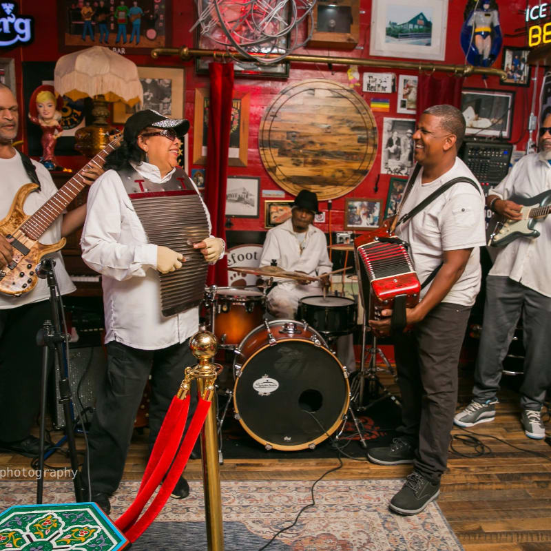 A band of musicians plays in a dimly lit room adorned with eclectic decor, with a red velvet rope in the foreground.