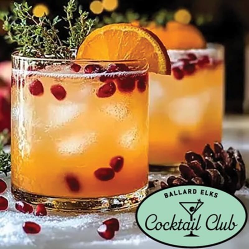 Two festive cocktails with orange slices and pomegranate seeds sit on a snowy surface in the foreground, with blurred holiday lights in the background.