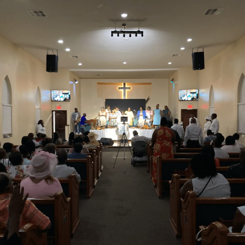 A choir sings on a stage in front of a cross in a church sanctuary, while a congregation sits in pews in the foreground.