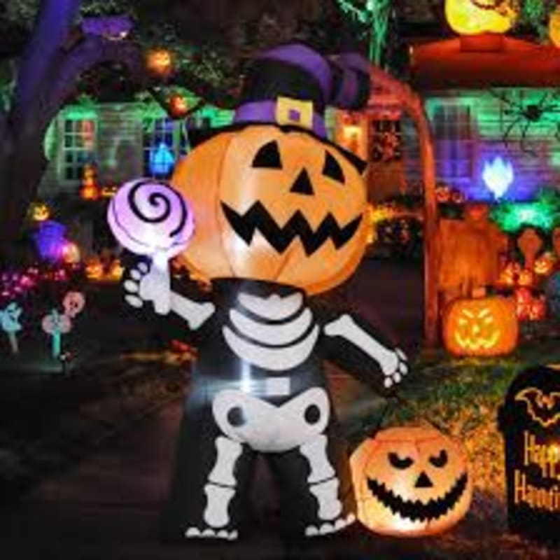 An inflatable pumpkin skeleton character holding a lollipop stands in the foreground, surrounded by glowing jack-o'-lanterns and Halloween decorations in the background.