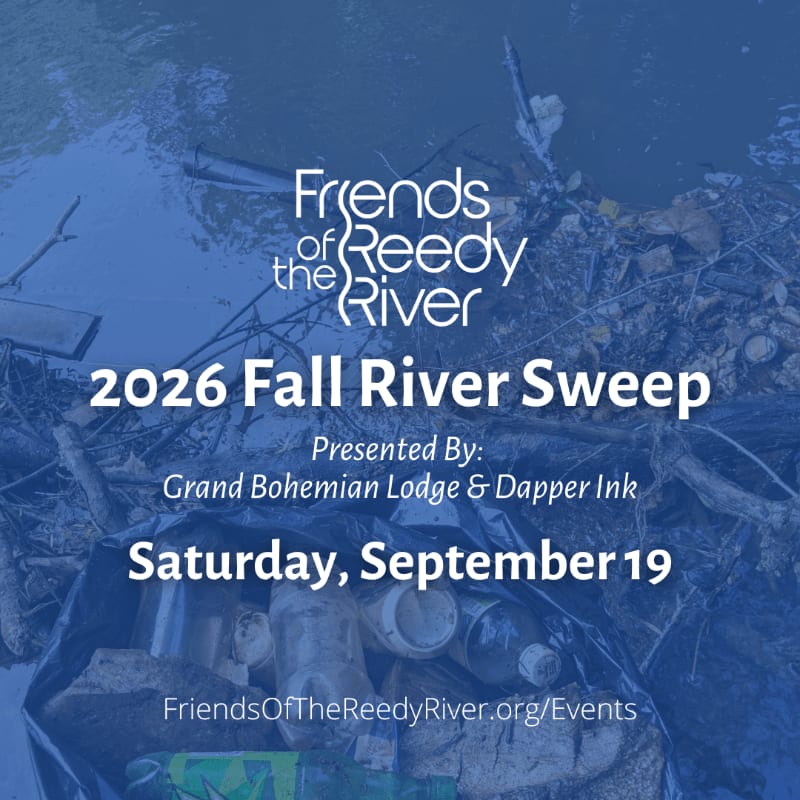 A black trash bag filled with collected debris sits in the foreground, while the murky water of the Reedy River, with scattered trash, forms the background.