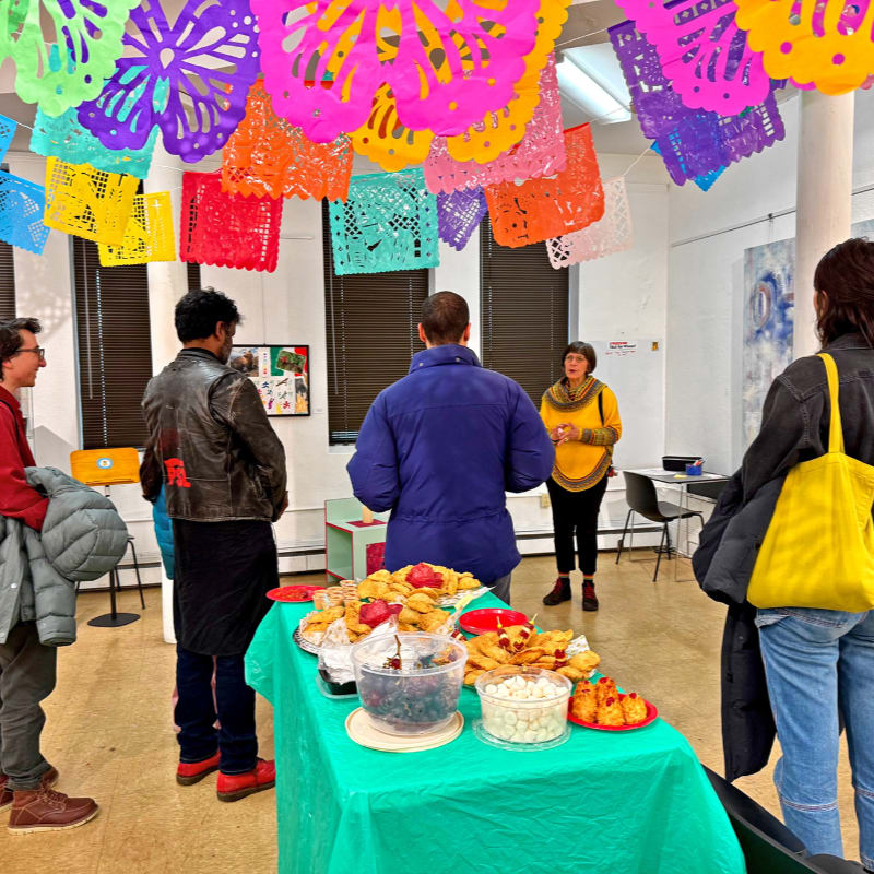 In the foreground, two young people with glasses are painting on a large, colorful abstract canvas, while the background is a plain, light-colored wall.