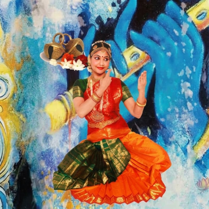 Four women in colorful traditional Indian attire perform a dance on a dark stage, with two in the foreground seated and adorned with garlands, and two in the background standing.