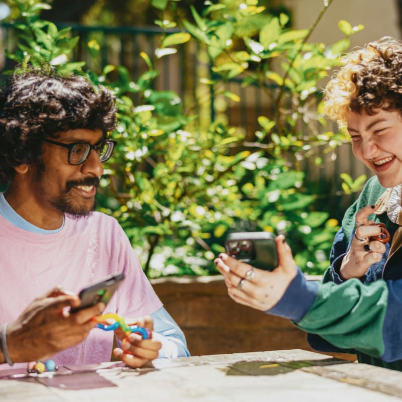 Two autistic friends sitting outside using stim toys and laughing at their phones