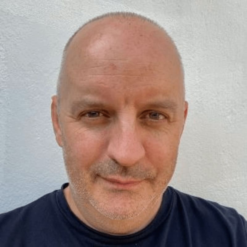 A bald man with a dark shirt smiles slightly in the foreground against a textured white background.