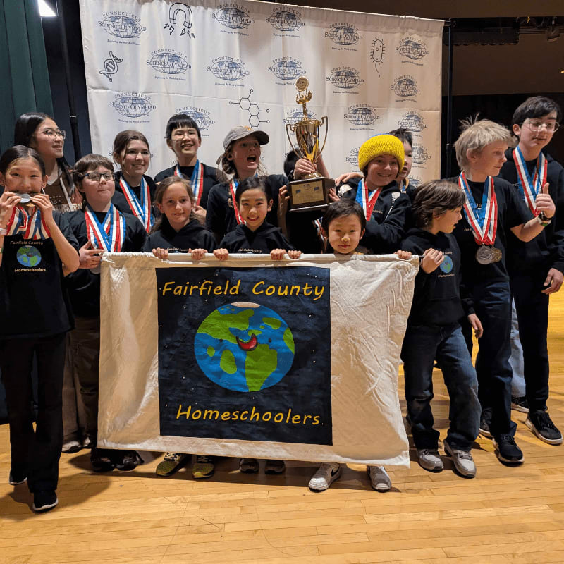 A group of children in the foreground hold a banner that reads "Fairfield County Homeschoolers" while a trophy is held aloft in the background.
