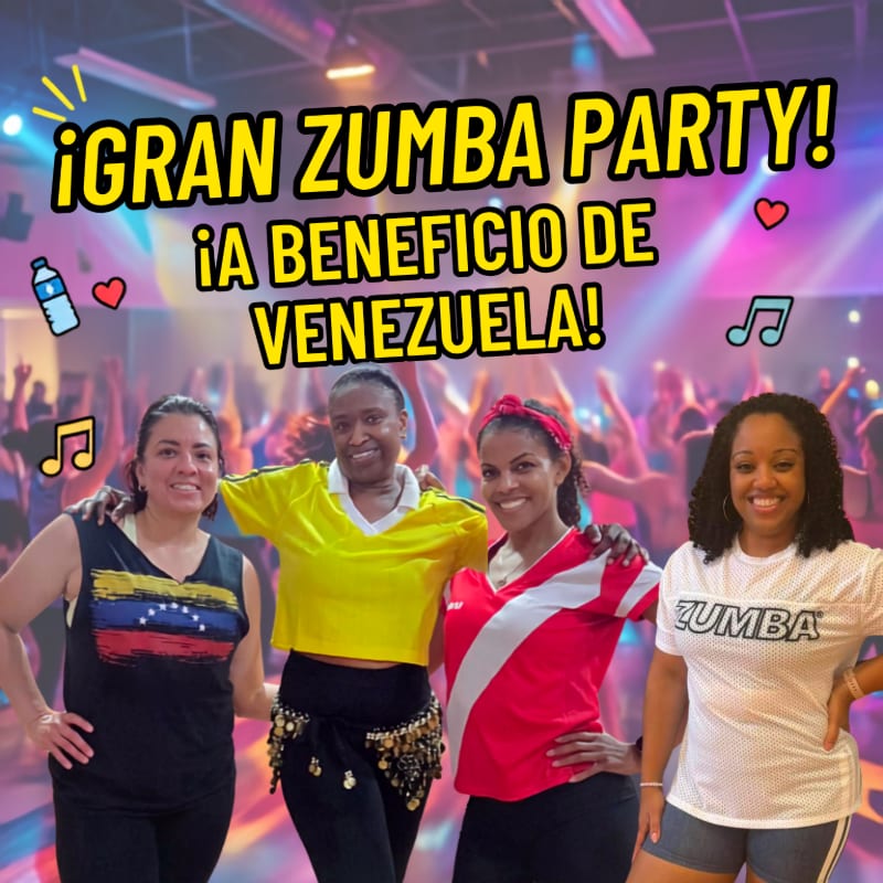 Four women smile in the foreground of a blurred background filled with people dancing at a Zumba party.