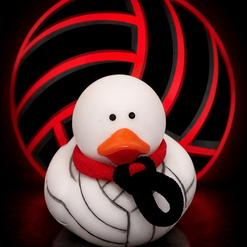 A white rubber duck wearing a red scarf stands in front of a glowing black and red volleyball.
