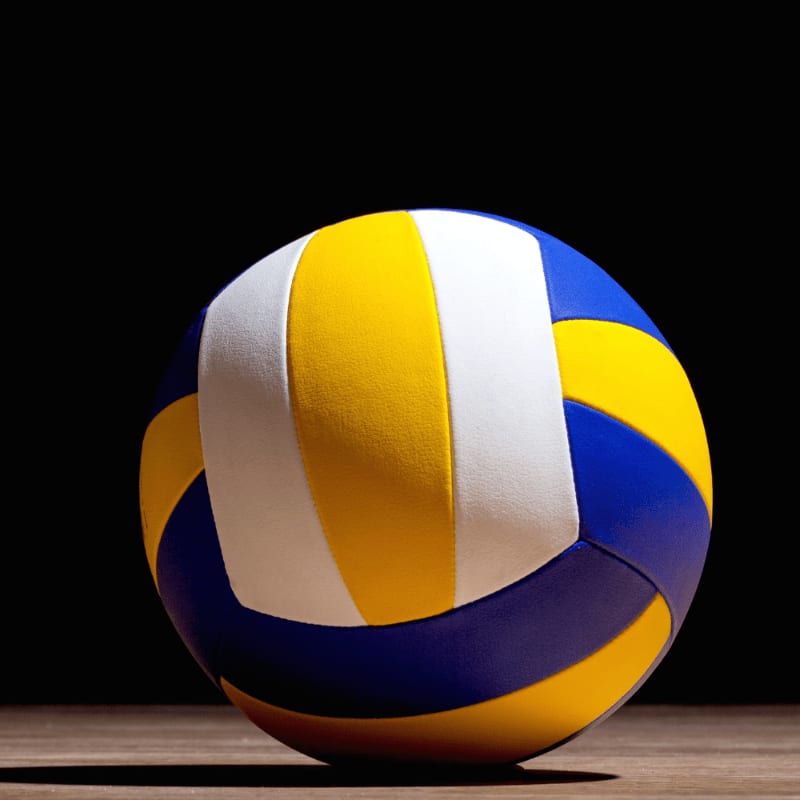 A colorful volleyball rests on a wooden surface against a dark background.