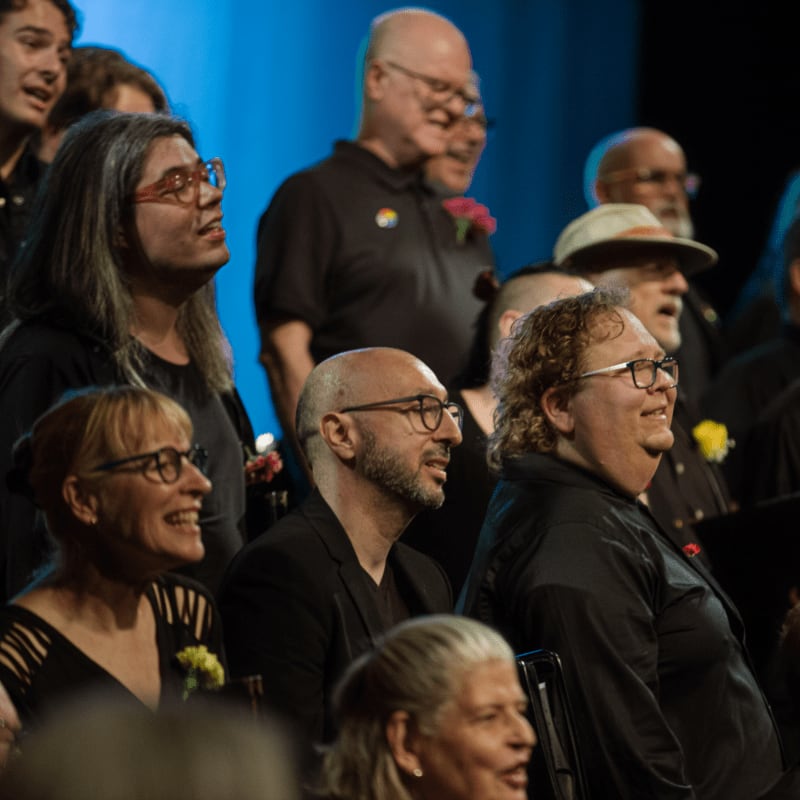 A diverse group of people, some wearing glasses and smiling, are gathered in front of a blurred blue background.