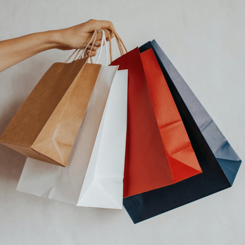 Hand holding colorful shopping bags against a light background