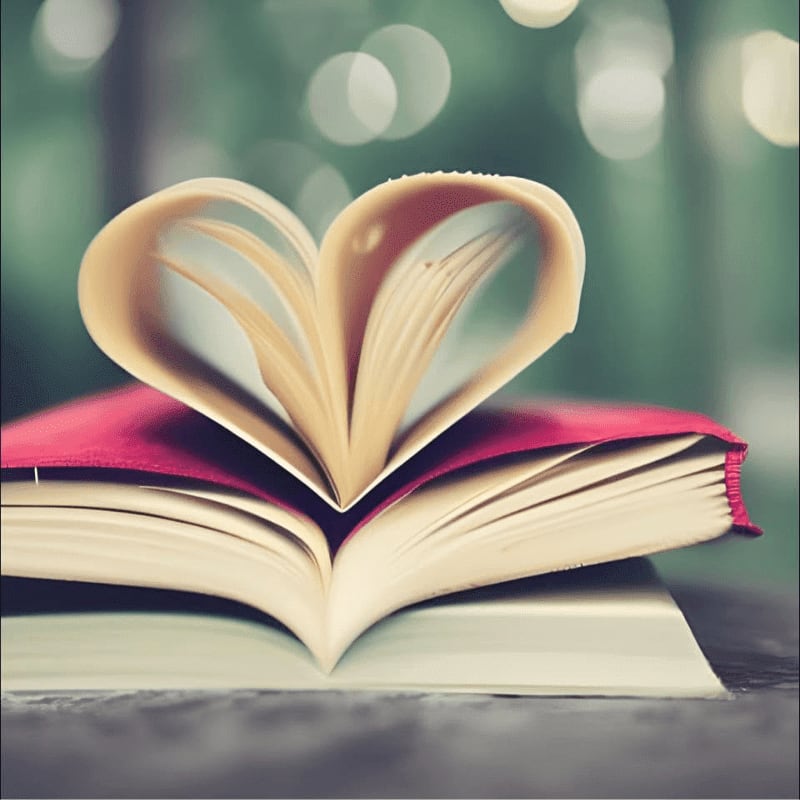 Pages of an open book are folded into a heart shape on top of a red book, with a blurred green background.