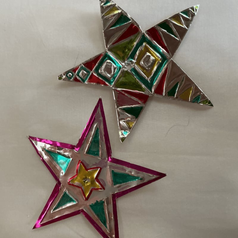 Two colorful, metallic star ornaments with geometric patterns are laid out on a white, textured surface.