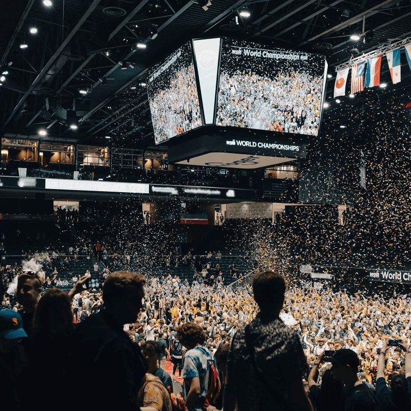 Confetti rains down on a cheering crowd in a stadium, with a large screen displaying "World Championships" above them.