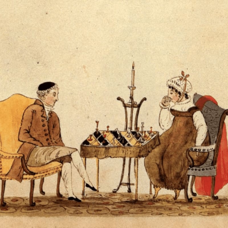 A man and a woman sit in chairs facing each other across a table with a chessboard and candle, against a plain, light-colored background.