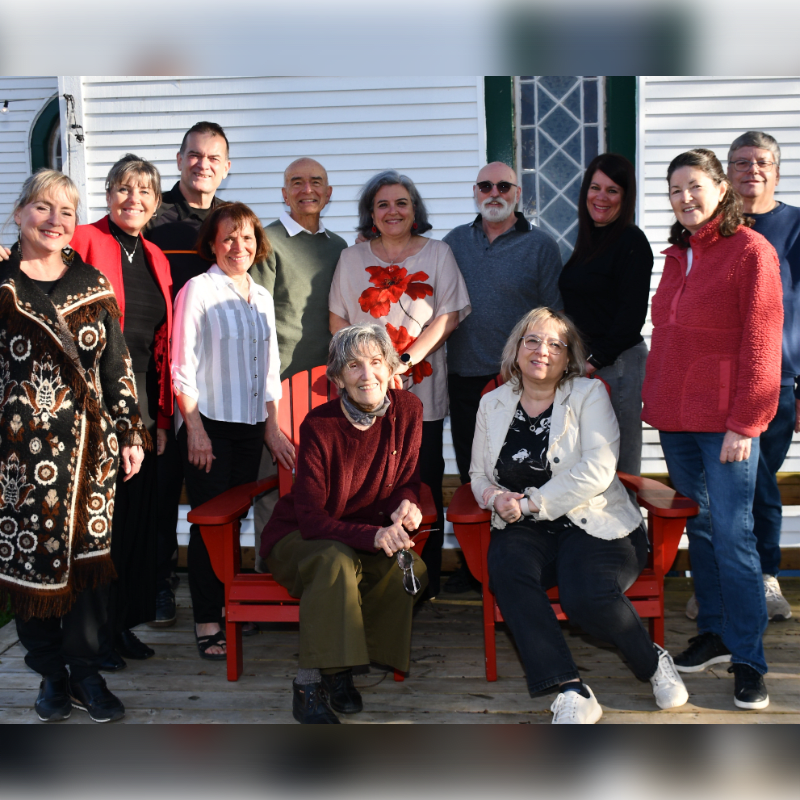 A group of people pose for a photo on a wooden deck in front of a white building.