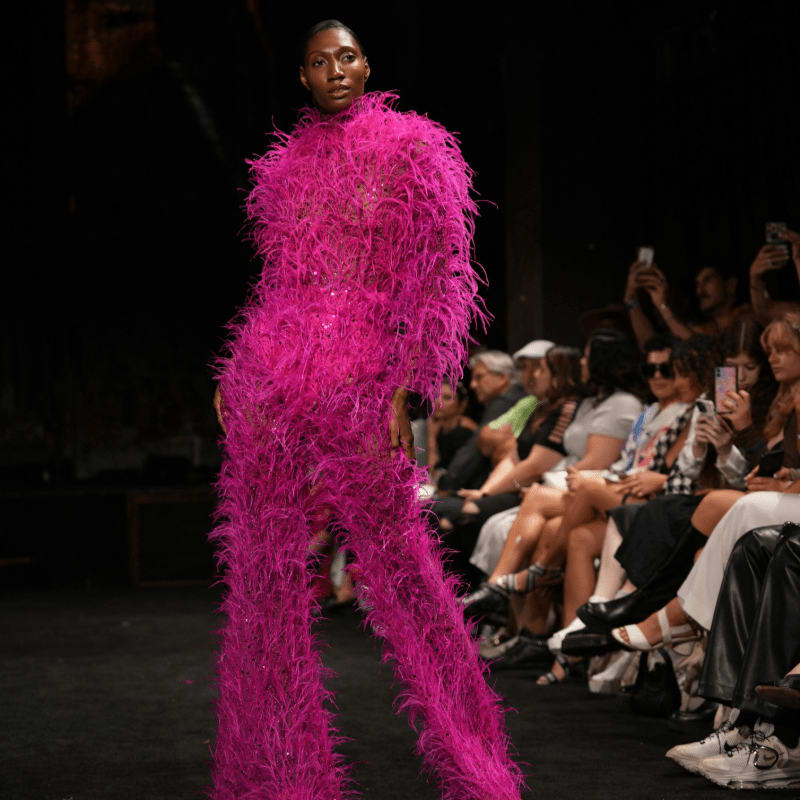 Model in a vibrant pink feathered outfit on a runway