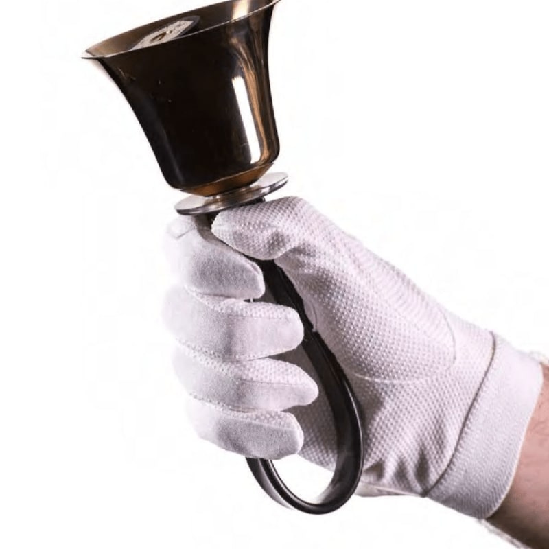A white-gloved hand holds a brass bell against a plain white background.