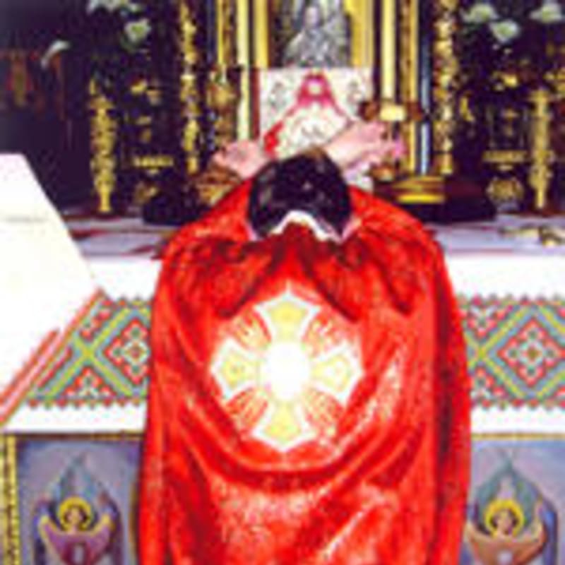 A person in a red ceremonial robe with a cross emblem bows before an ornate altar in a church.