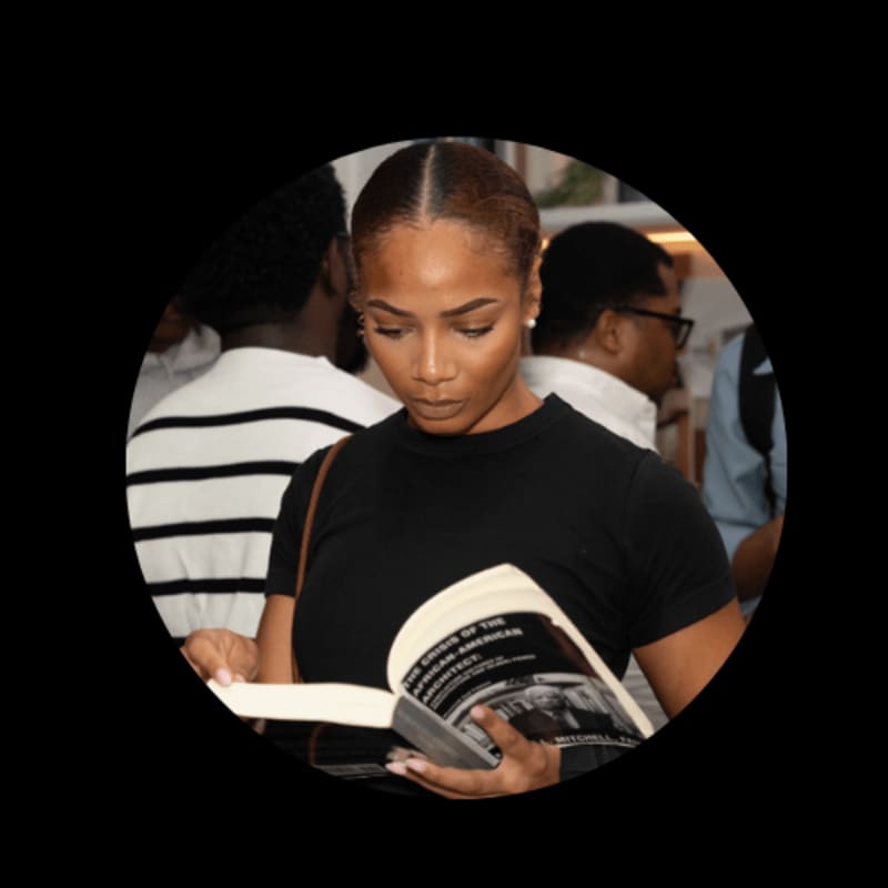 A woman in a black shirt reads a book in the foreground, with blurred figures in the background.