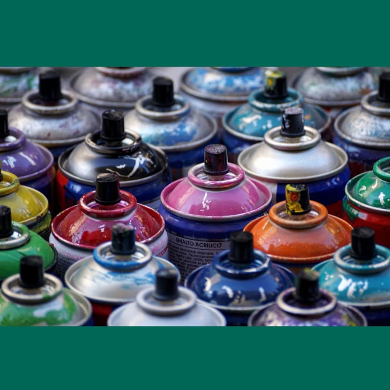 A colorful collection of spray paint cans fills the foreground, with more cans blurred in the background.