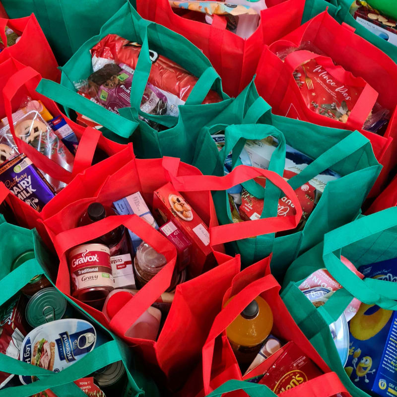 Many reusable red and green shopping bags filled with various food items