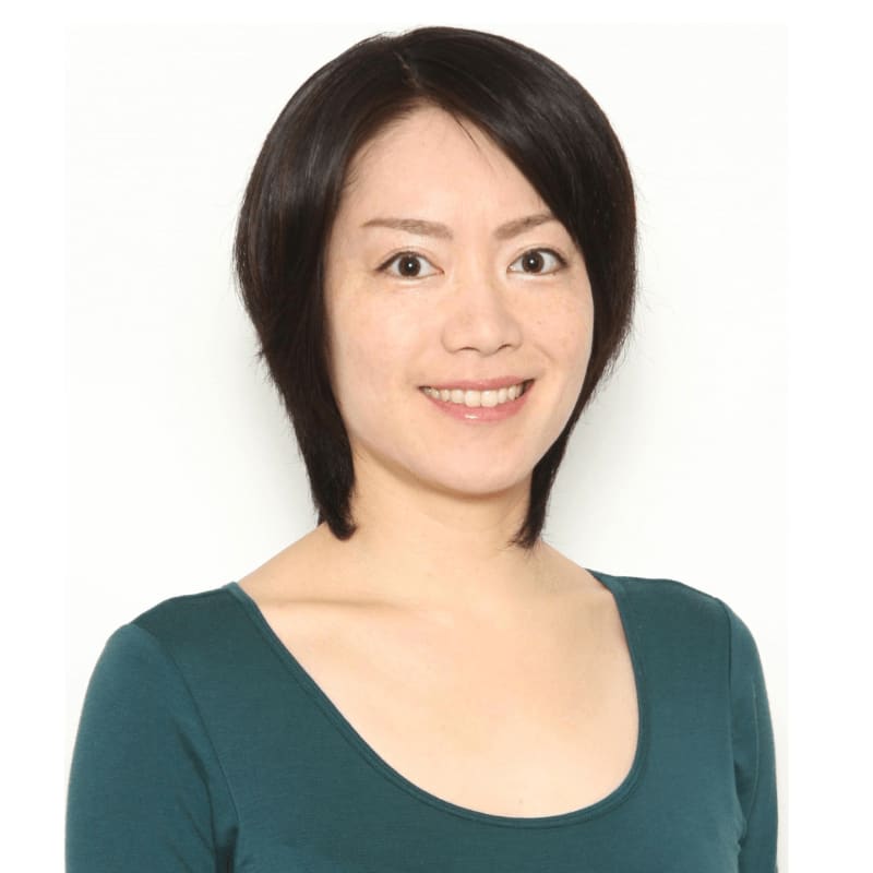 A smiling woman with short black hair and a teal shirt is in the foreground, set against a plain white background.