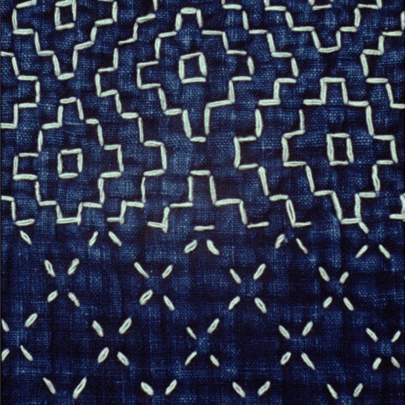 White geometric stitching forms a repeating pattern on a dark indigo fabric background.
