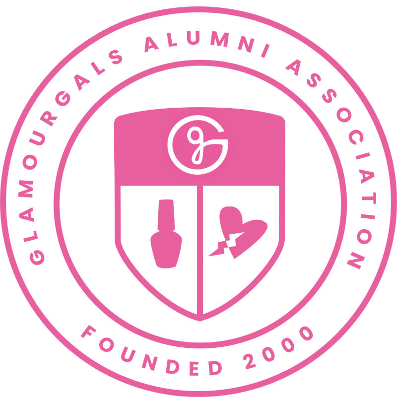 A pink circular emblem with "GLAMOURGALS ALUMNI ASSOCIATION FOUNDED 2000" encircling a shield containing a stylized "G", a nail polish bottle, and a broken heart.