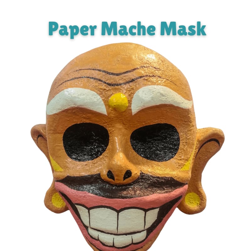 A colorful, grinning paper mache mask with large black eyes and a pink mouth is centered against a plain white background.