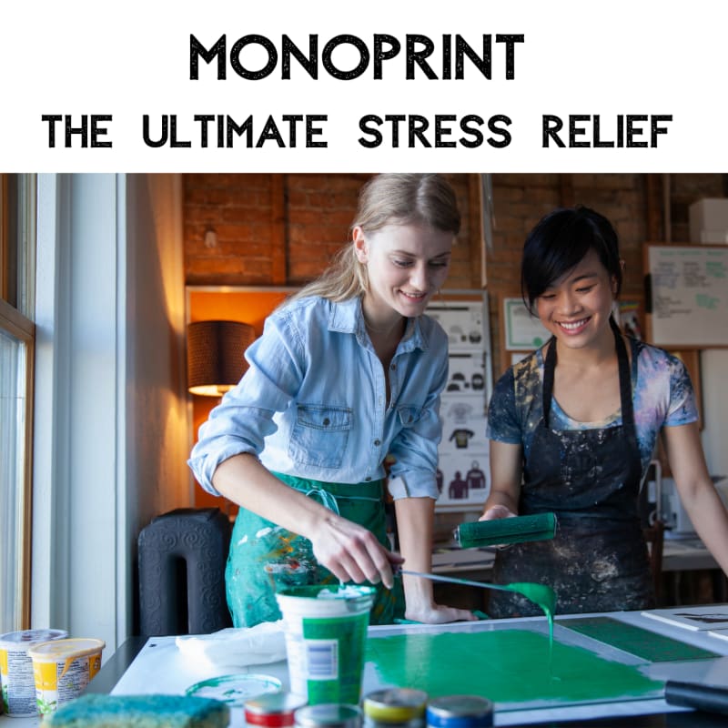 Two women are happily engaged in a monotype printing process in a studio, with art supplies and a window visible in the background.