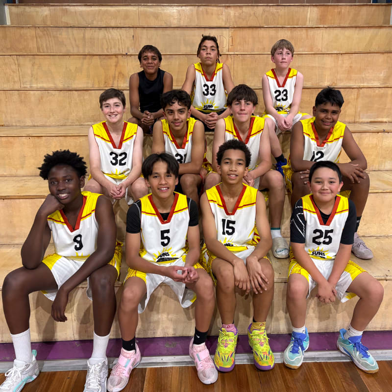 A group of young basketball players in yellow and white uniforms pose on bleachers in a gymnasium.