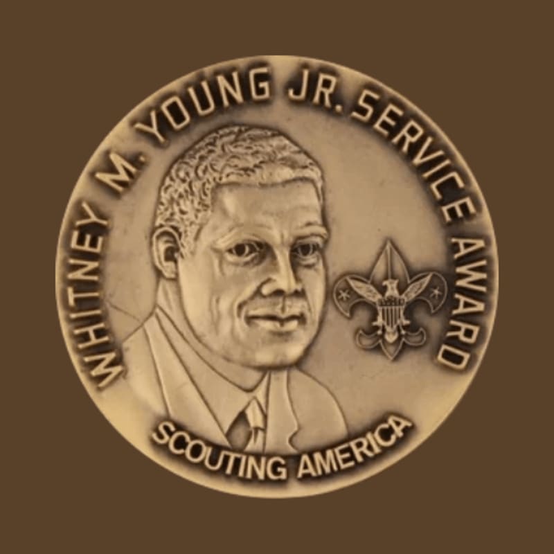 A bronze medal featuring a relief portrait of Whitney M. Young Jr. and the Scout emblem is set against a dark brown, textured background.