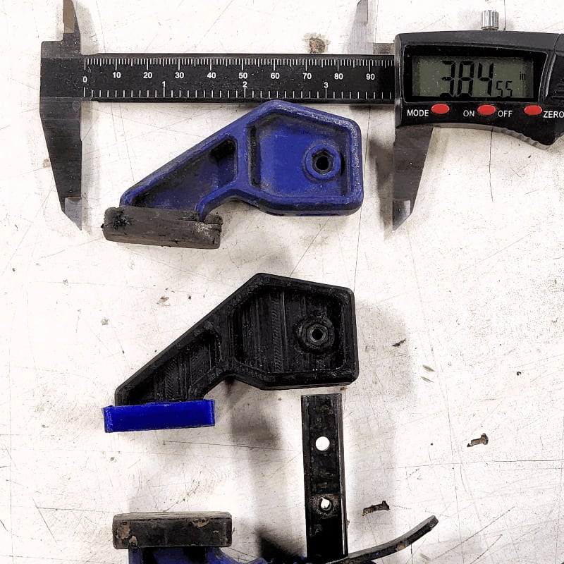 A digital caliper measures a blue clamp in the foreground, while a black clamp lies disassembled in the background.